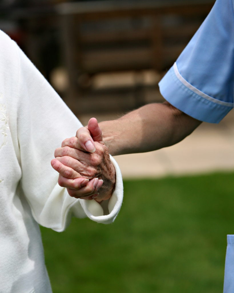 Carer and resident from Heaton House specialist dementia care home holding hands in the garden.